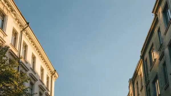 Weiter Himmel ist zwischen zwei schlichten Hausfassaden zu sehen.