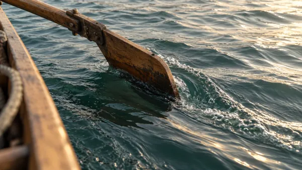 Ein hölzernes Bootsruder lenkt durch strömendes Wasser; daneben zieht die Strömung ruhig vorbei.